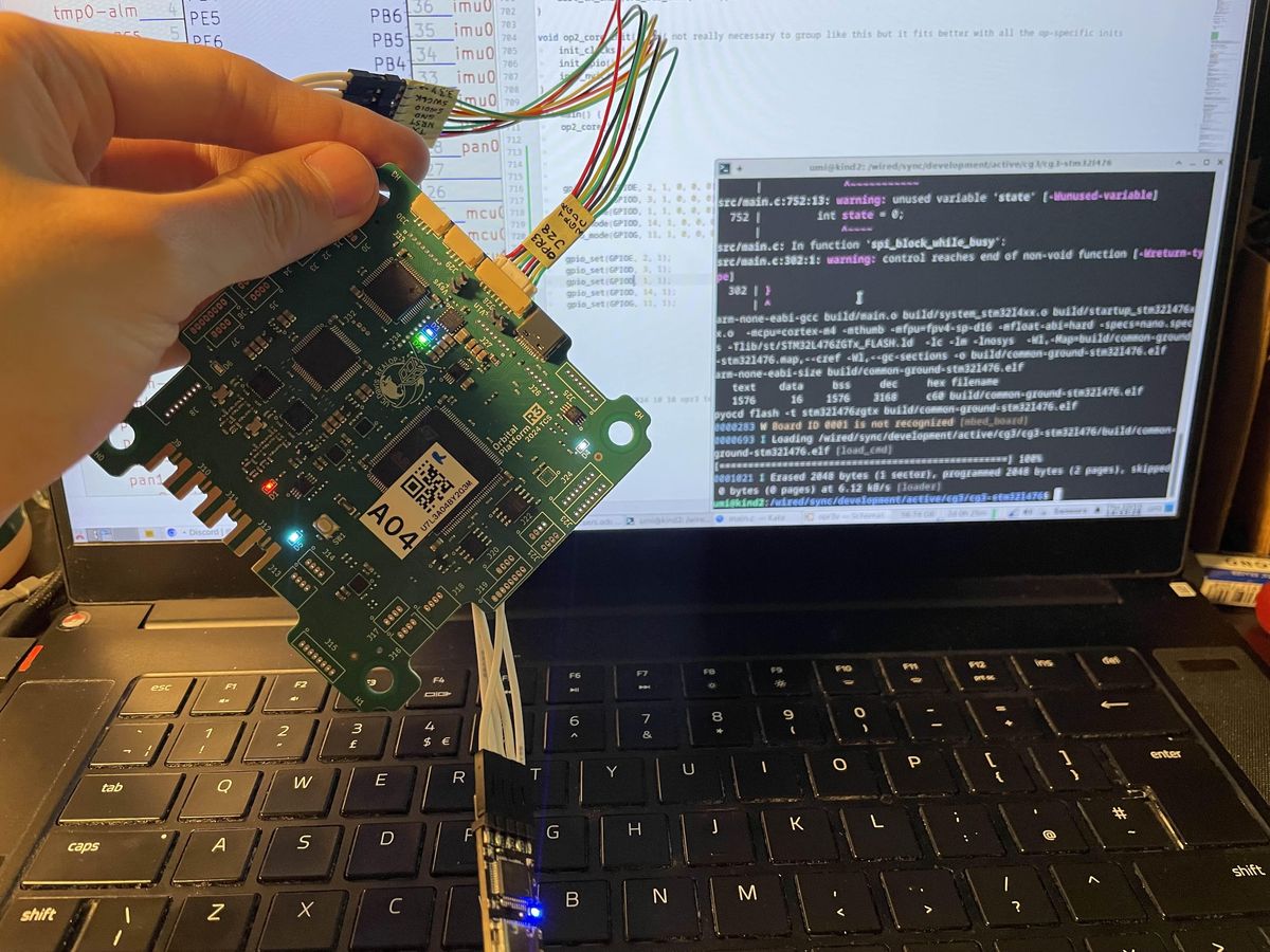 Flight computer PCBA held up while firmware flashes on a laptop